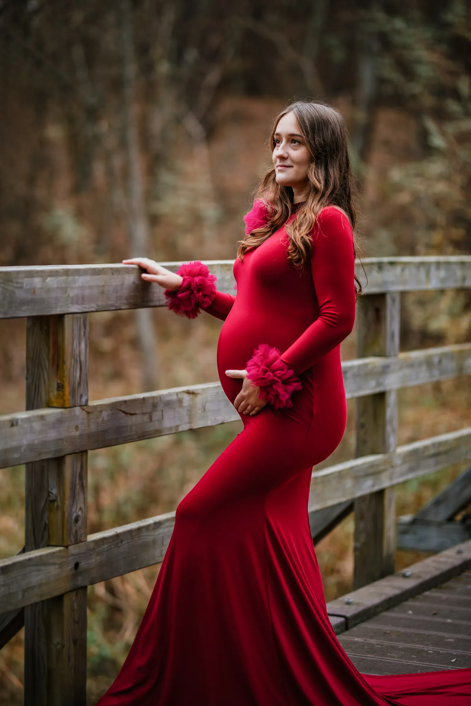 Przyszła mama w eleganckiej czerwonej sukni podczas sesji ciążowej